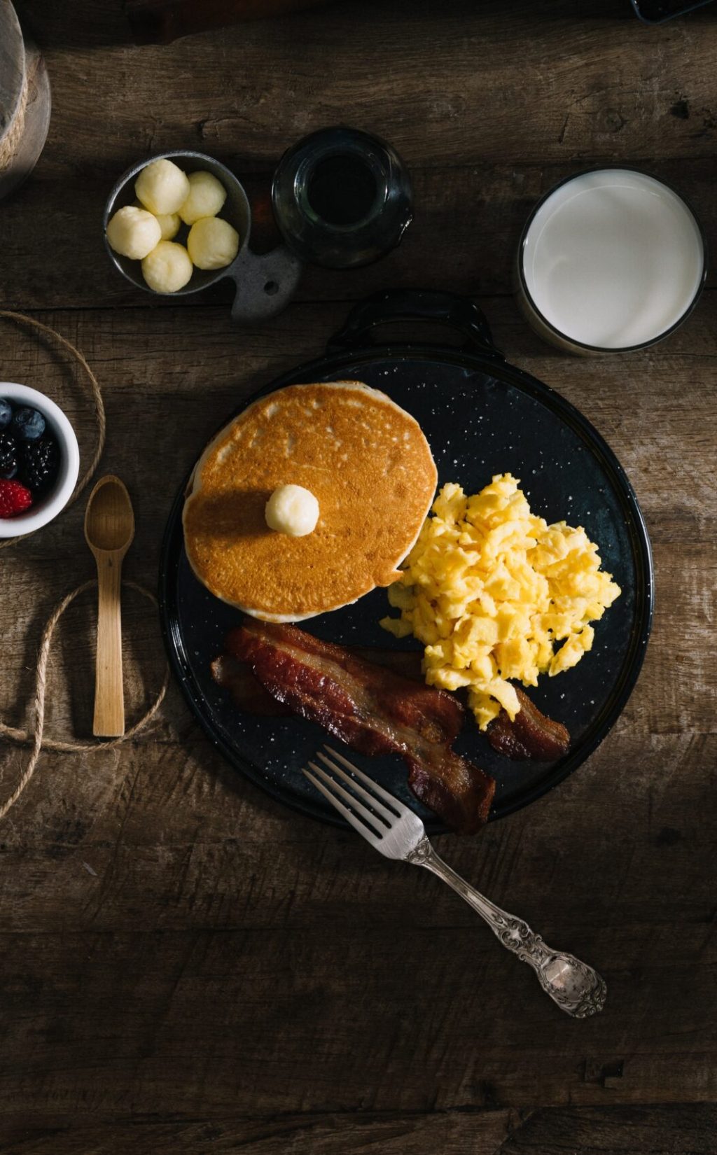 Rustic breakfast tablescape with pancakes, eggs, and bacon. Original public domain image from Wikimedia Commons